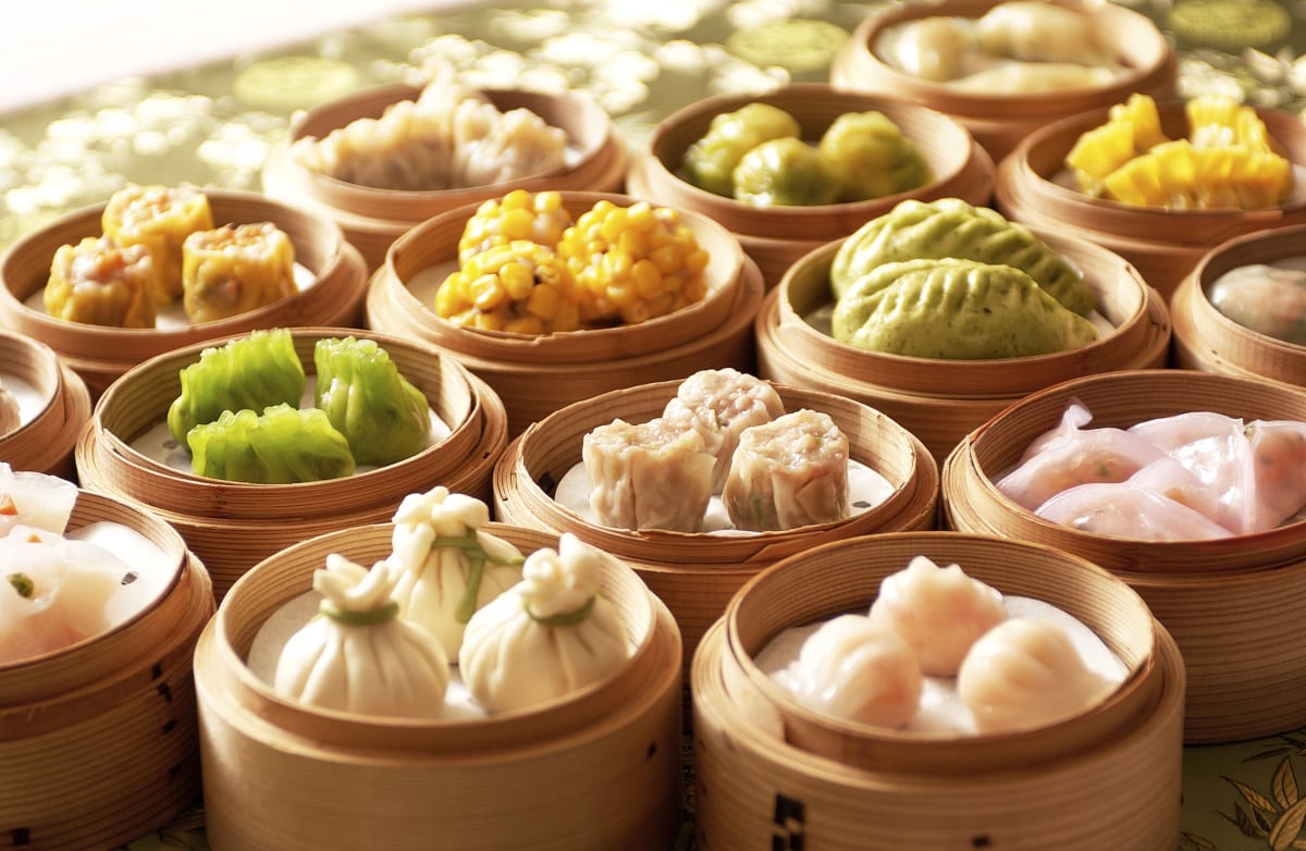 Dim Sum in bamboo steamers. Lots of different coloured dishes, like green dumplings, fish and a variety of vegetables on round bamboo steamer baskets. 