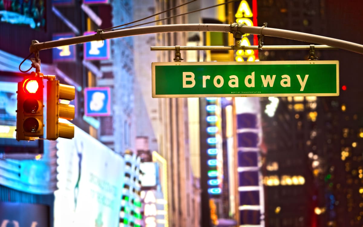 Broadway street sign in focus, with stop lights and broadway lights blurred in the background. 