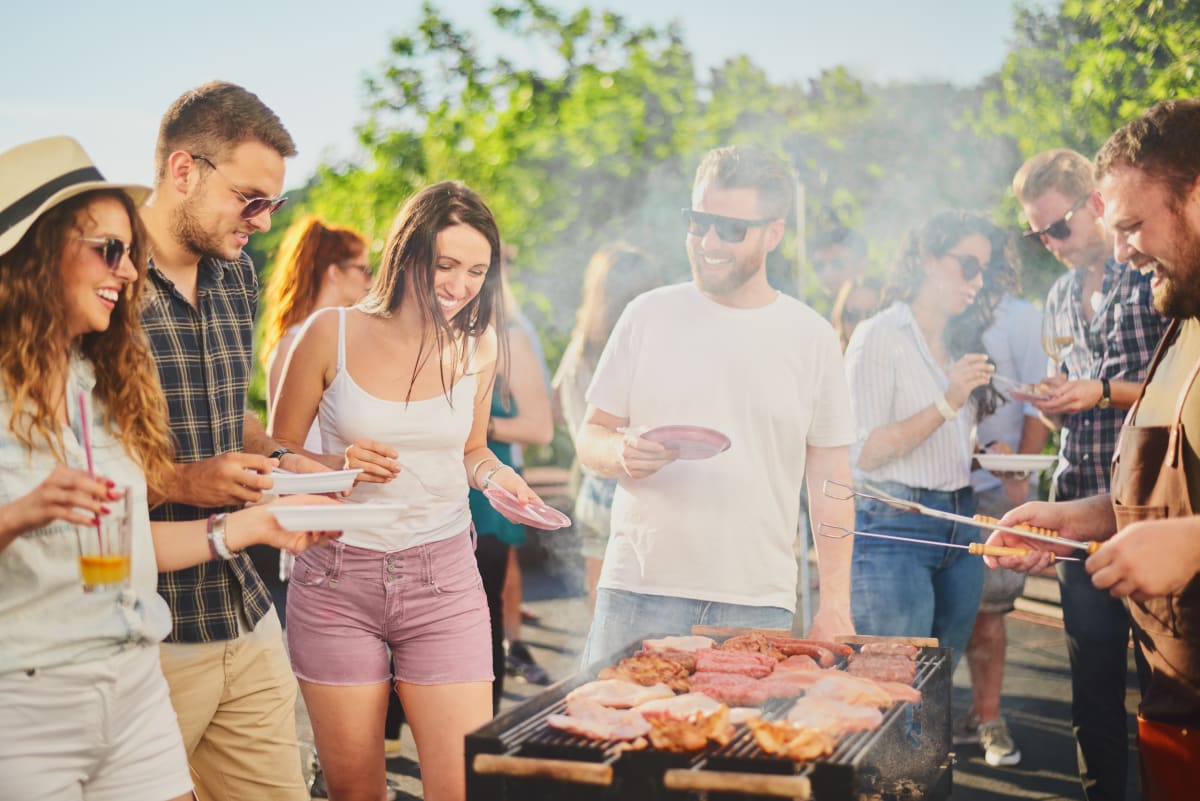 friends enjoying a bbq outside in the sun. Meat on the bbq, drinks in hand. 