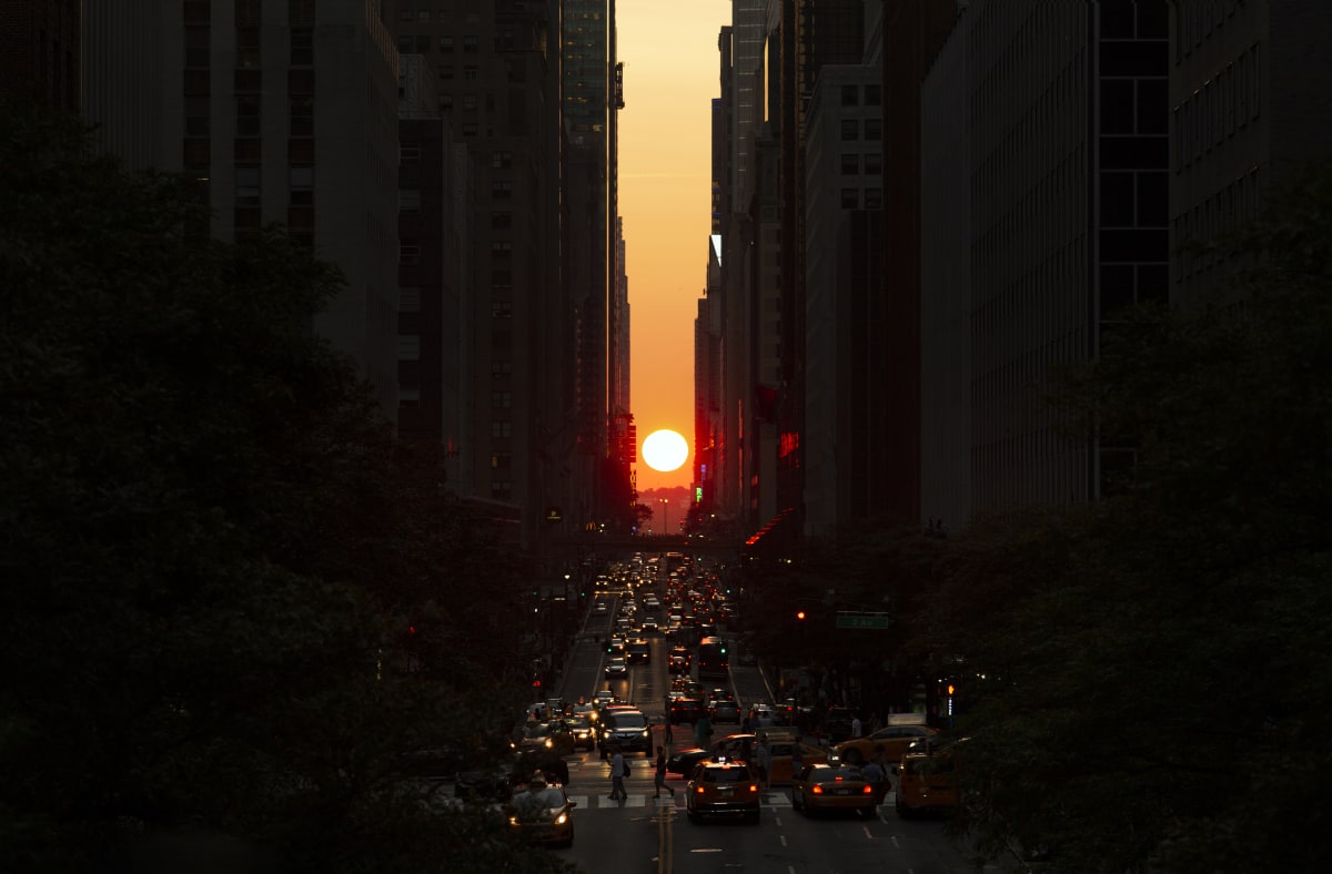 Setting sun between sky scrappers with traffic on the roads beneath 