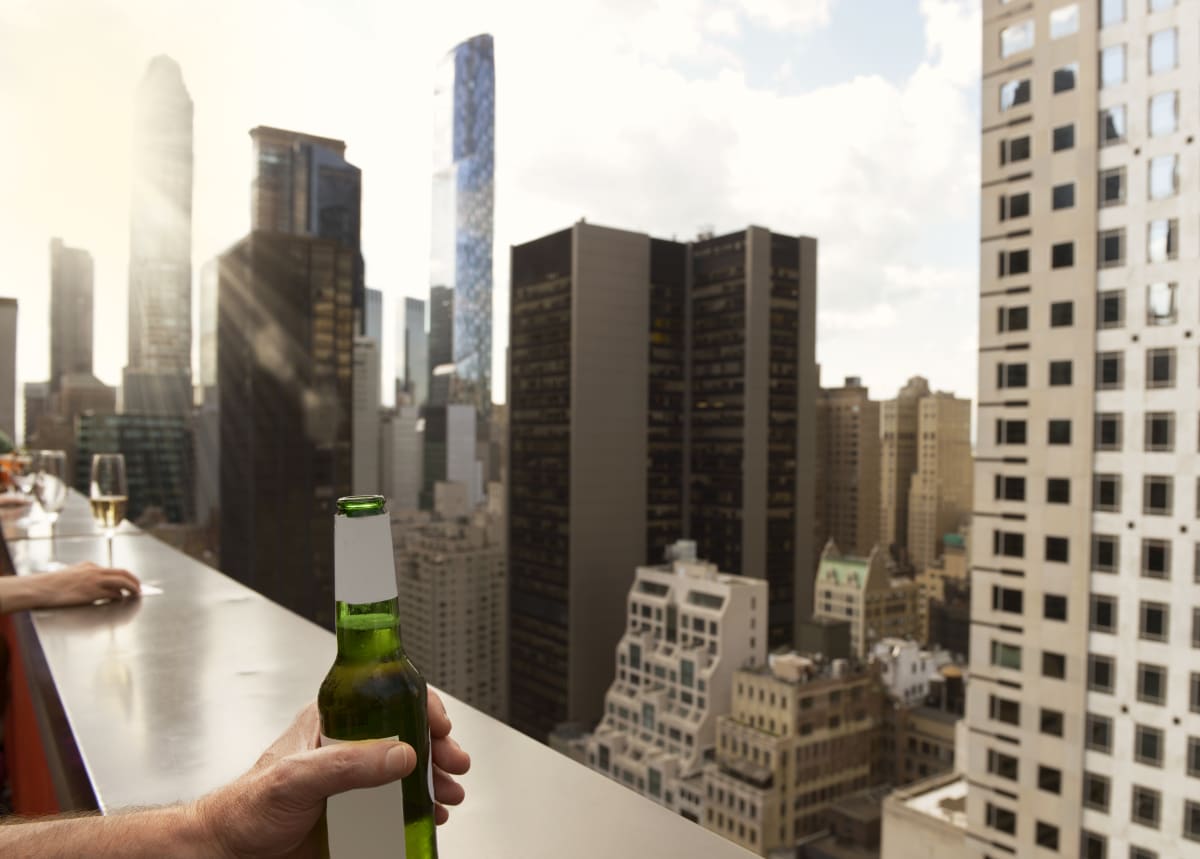 Roof terrace bar in new york, sky scrapers are in the background and a hand holds a beer. 