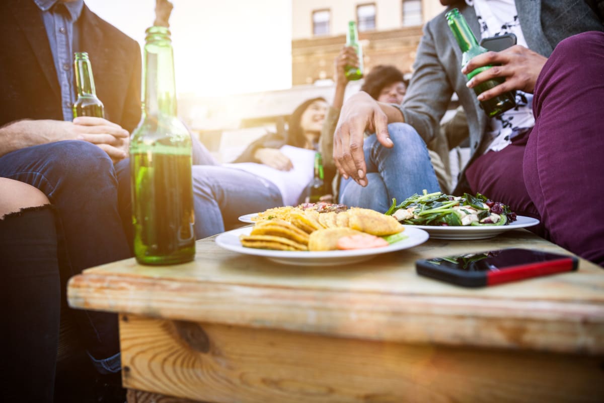 close up of an outdoor table in a bar, with snacks and bottled beers, friends sit around the table out of focus