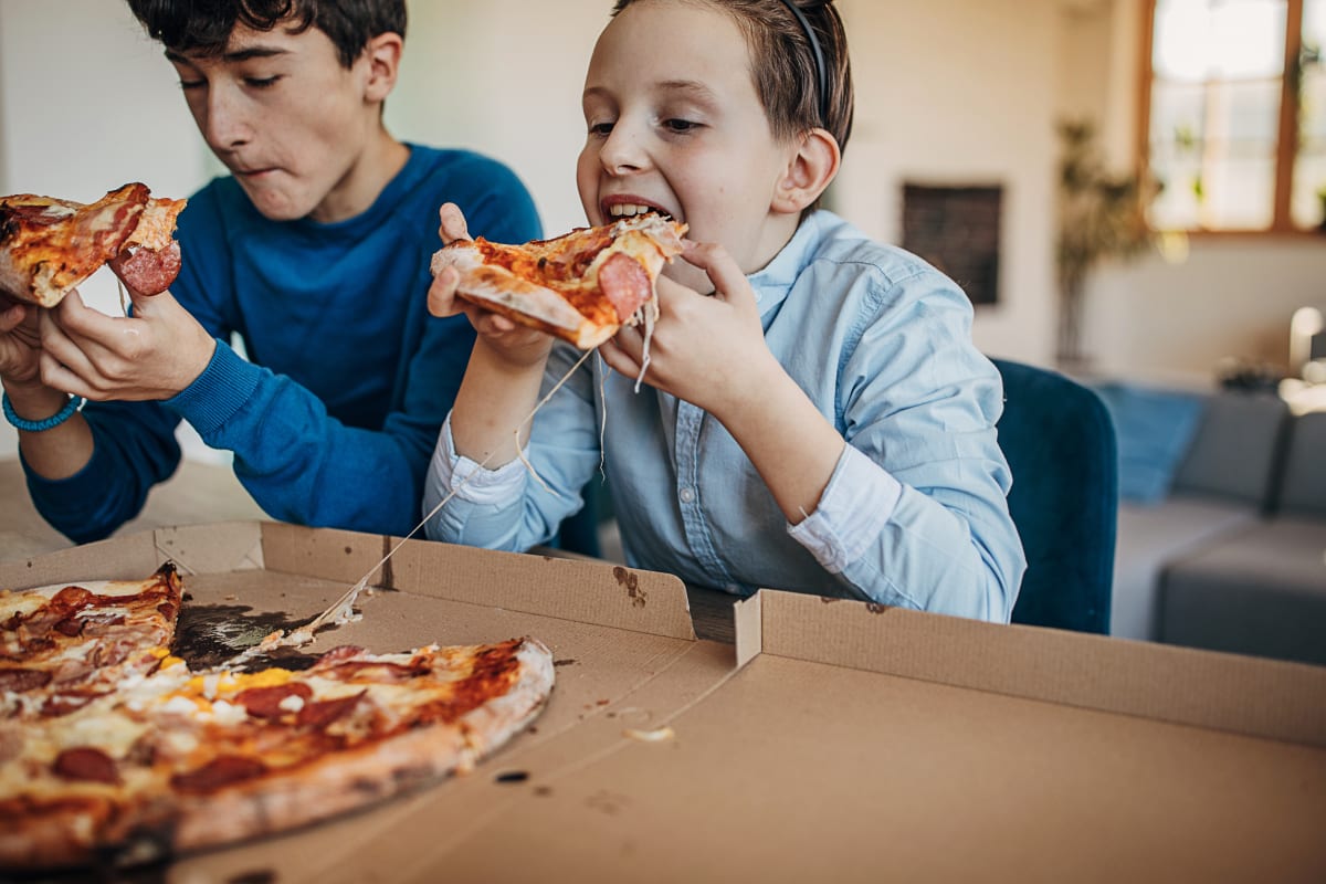 two children eat slices of pizza at a table in a home or hotel