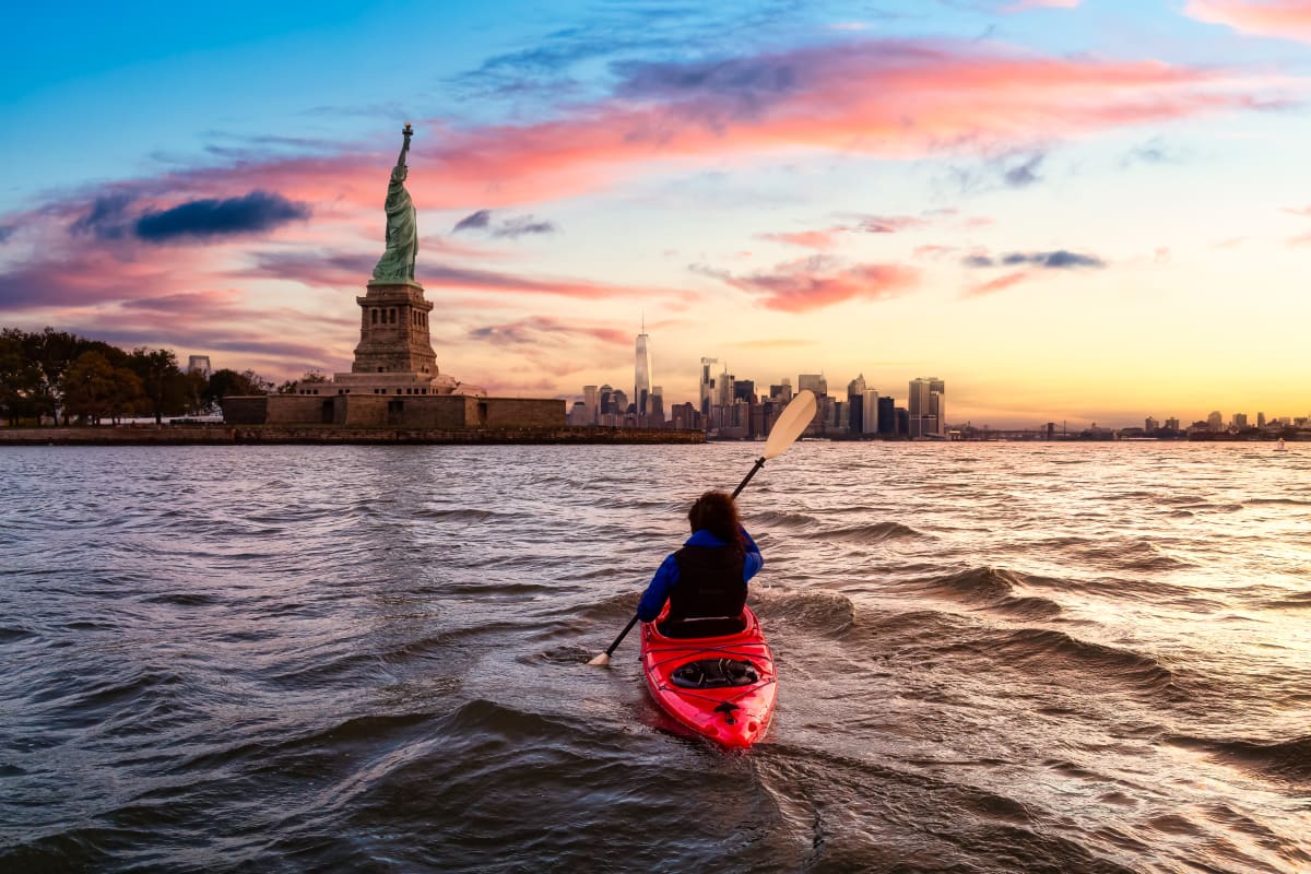 Loan kayaker in the water at sunset in front of the Statue of Liberty 