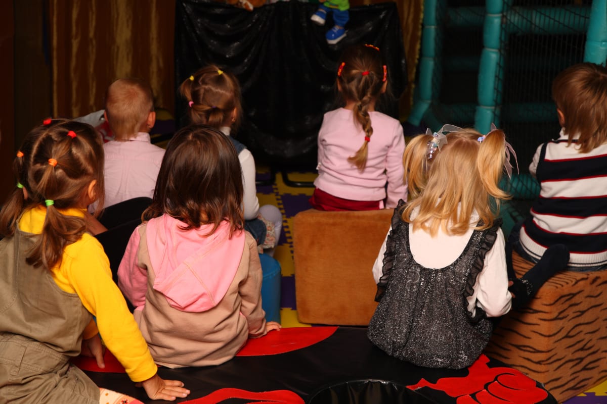 The backs of children's heads as they watch a puppet show in Central Park 