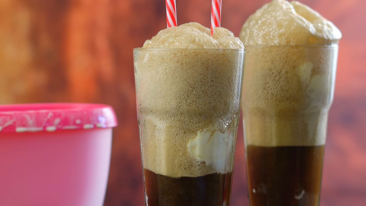 traditional coke float, with lots of foam on top and red and white striped straws inside, small pink plastic tub to the side of them 