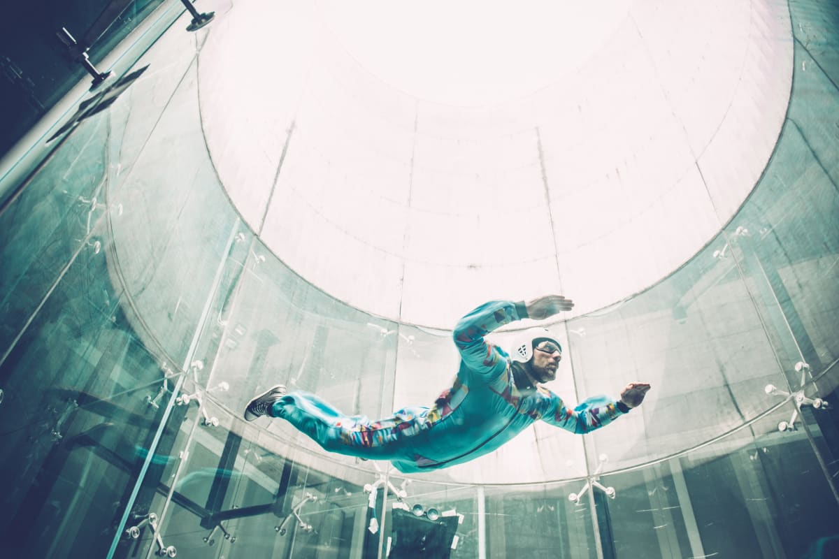 indoor sky dive, man floats in cylinder wearing googles and a helmet 