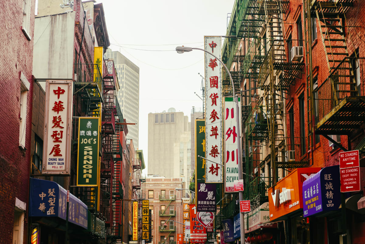 Street in Chinatown New York, looking up at buildings with large signs in Chinese letters advertising restaurants and shops. 