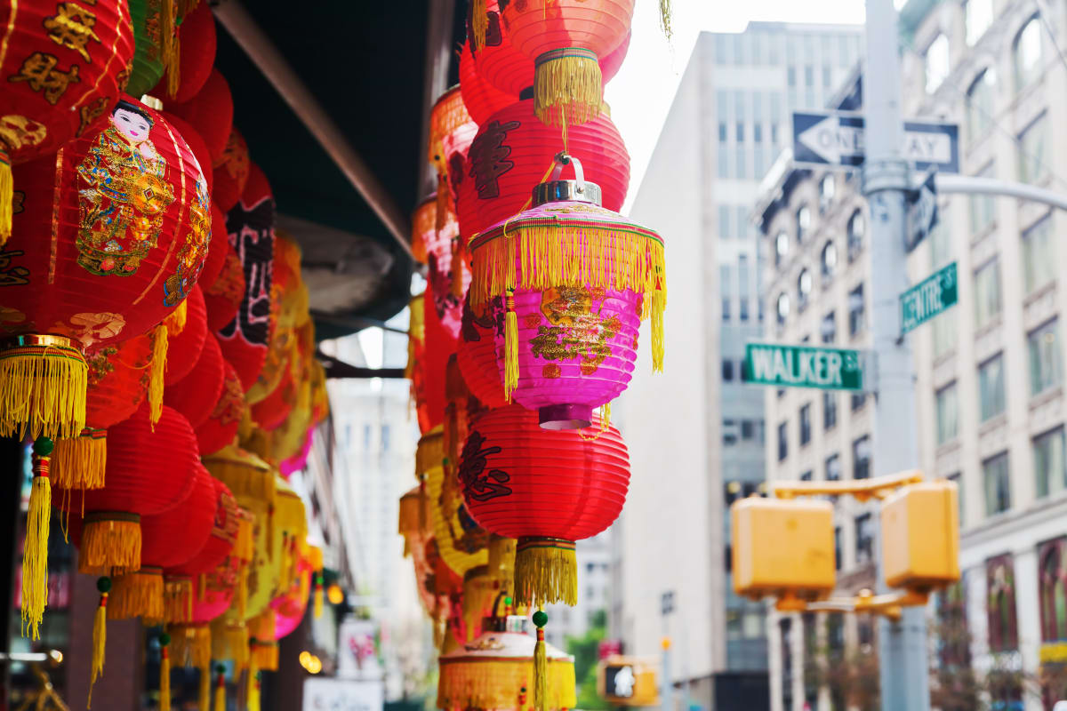 Traditional Chinese lanterns in red and pink with yellow trim hang outside a shop or restaurant on busy New York street 