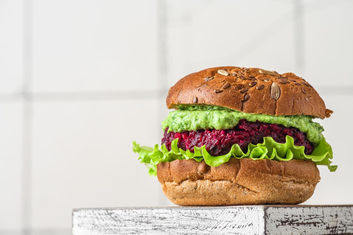 Vegan burger, seeded bread bun with a layer of lettuce, a thick deep pink vegan patty and a thick spread of guacamole. 