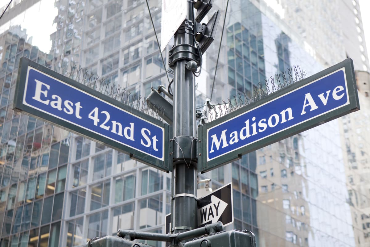 Street sign, with sign for Madison Ave and East 42nd St with skyscrapers in the background