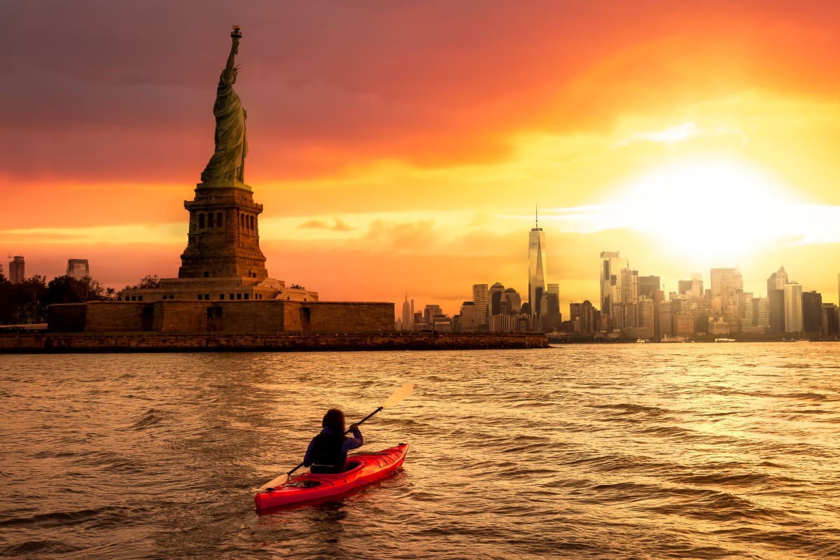 person kayaks in the water with the statue of Liberty and the Manhattan skyline in the background 