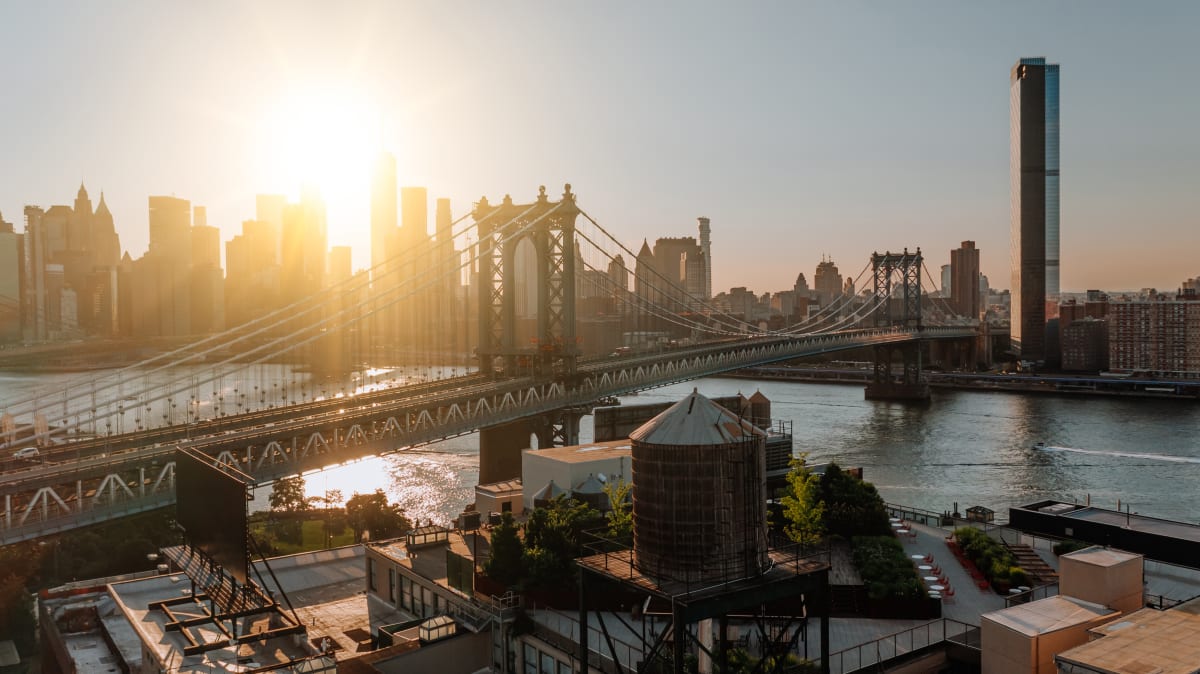 Manhattan Bridge, with the Hudson River and Manhattan Skyline in the background, with the sun appearing between the skyscrapers