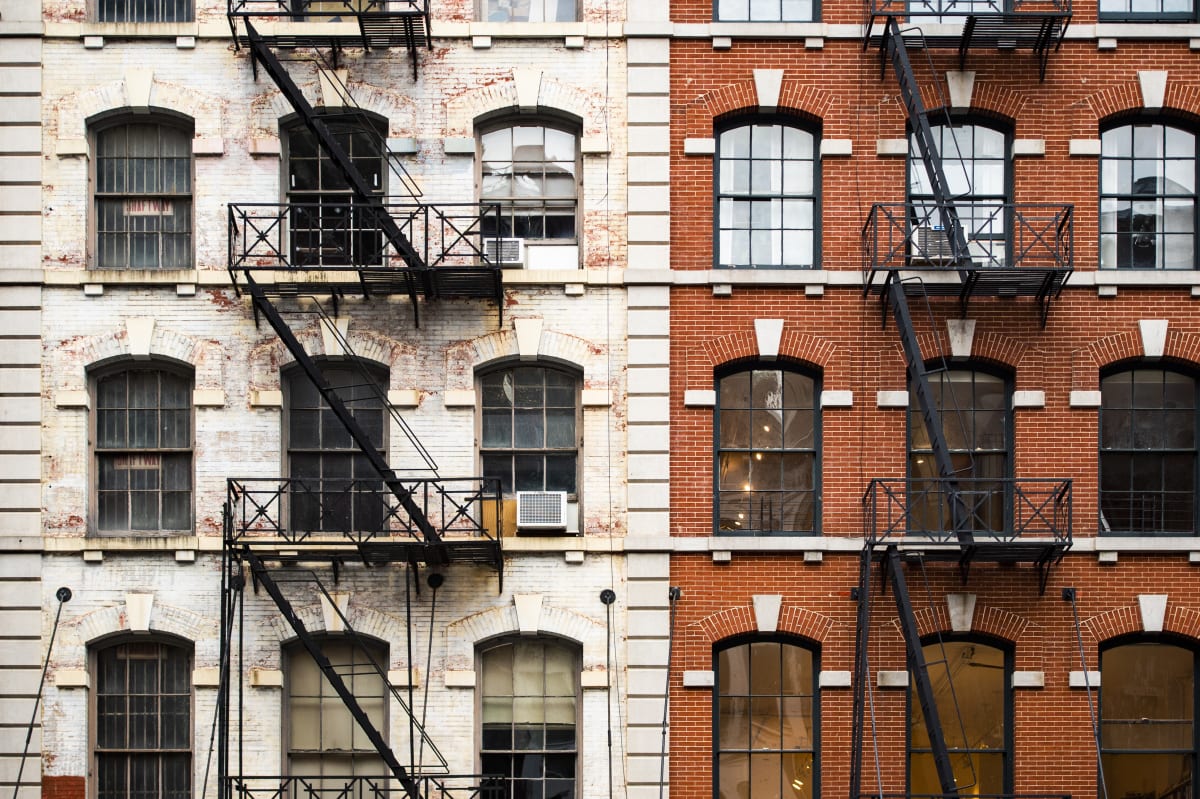 Two traditional New York residential blocks - one red brick, the other painted white - with traditional new york fire escapes