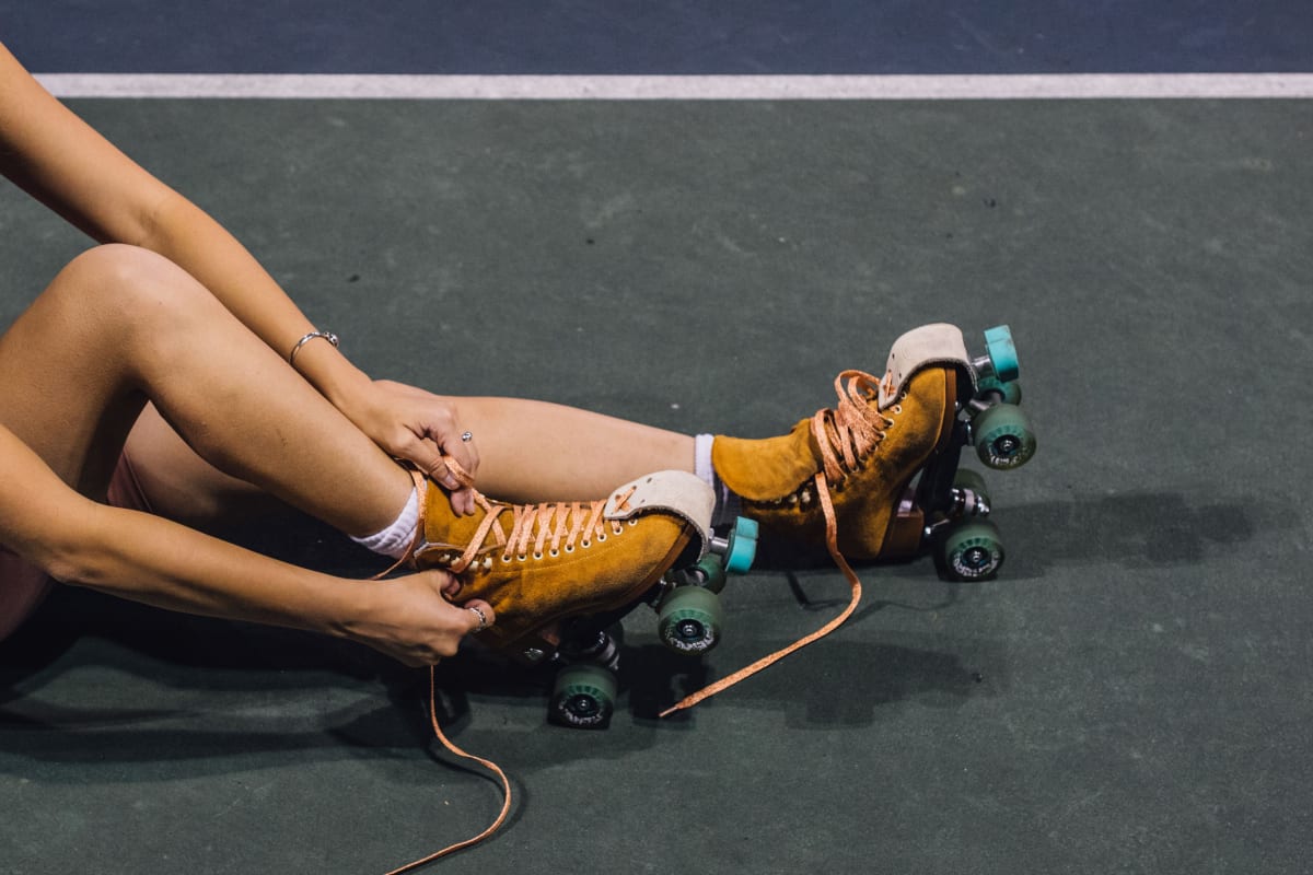 Legs of someone sitting on the ground and putting old school roller skates on 