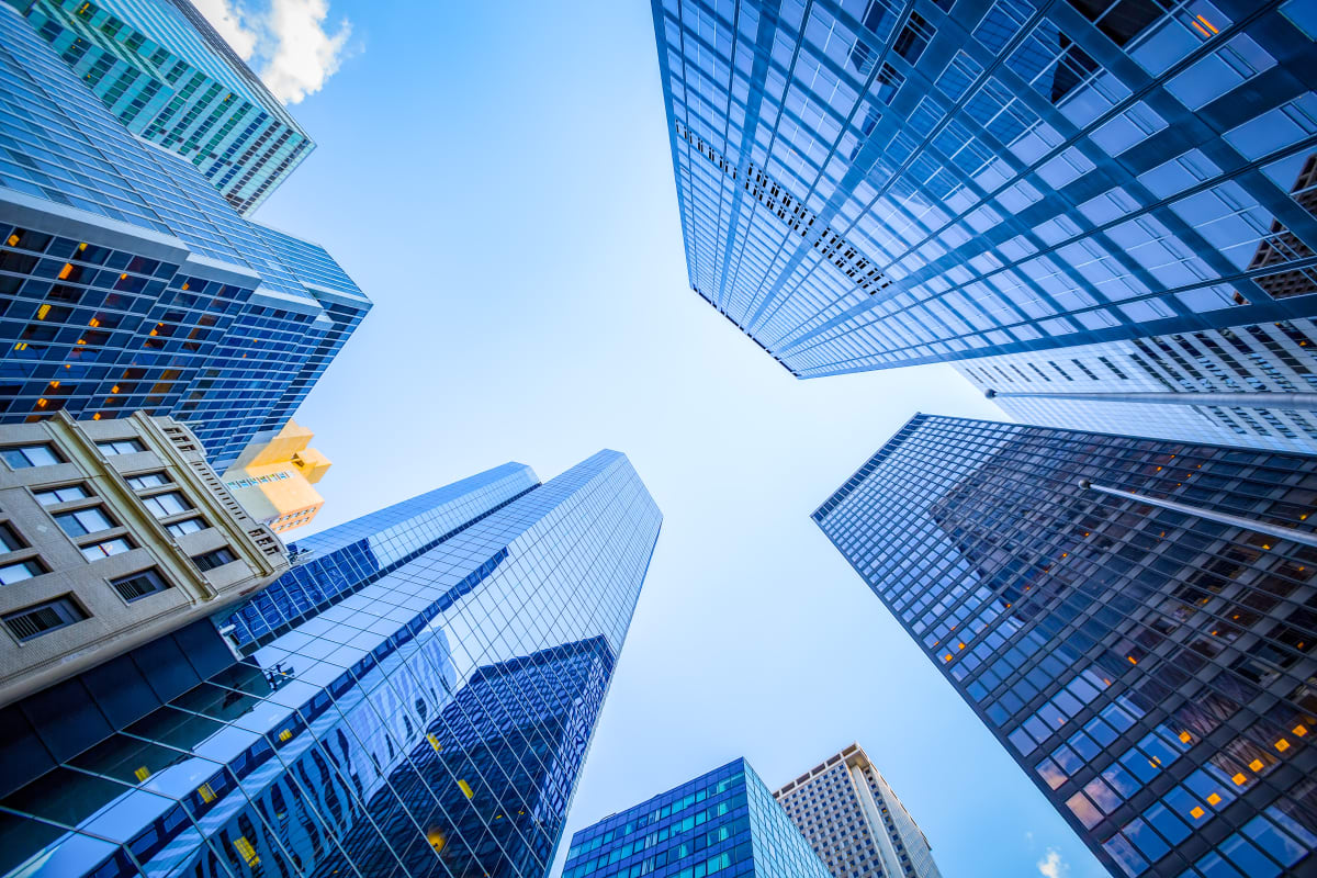 Looking up at tall skyscrapers from the ground, with blue skies in the middle 