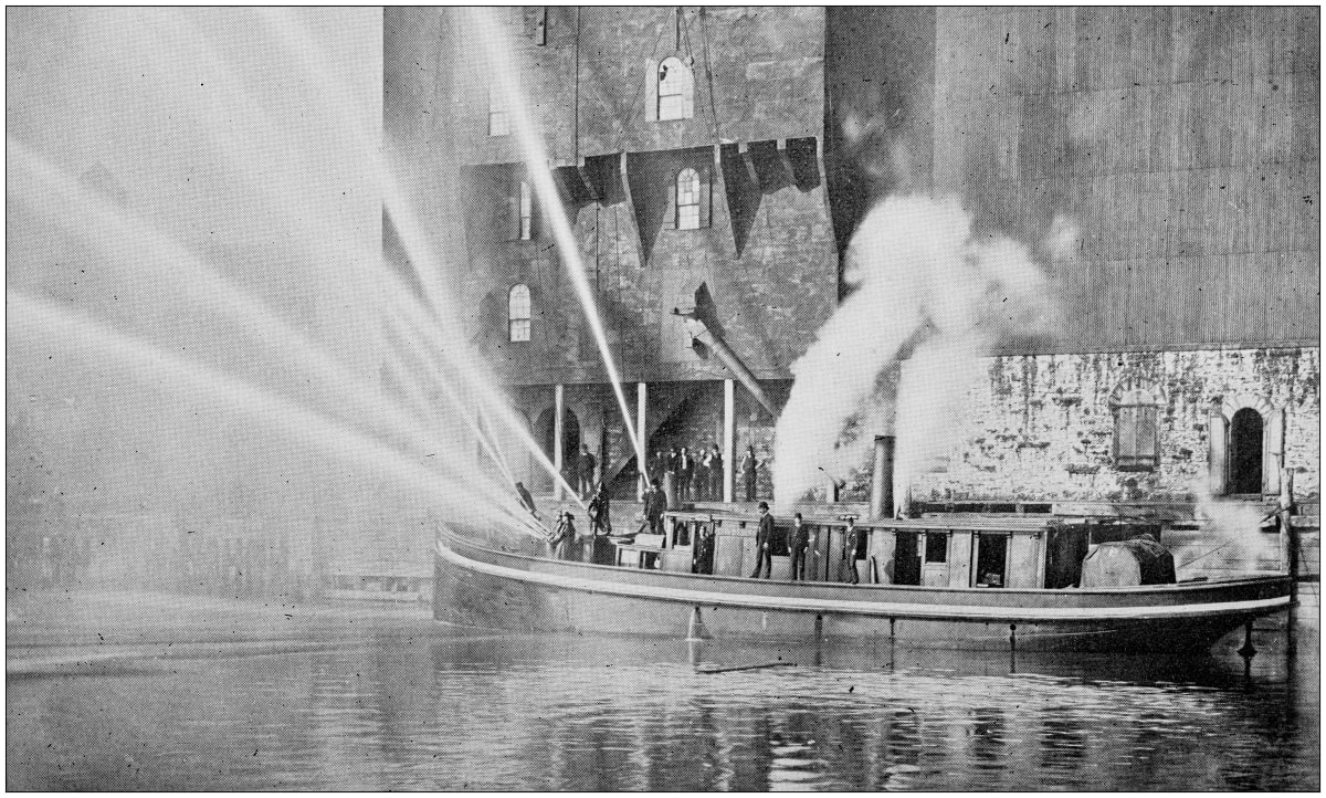 Black and white photo of old New York fire department putting out building fire from boat 