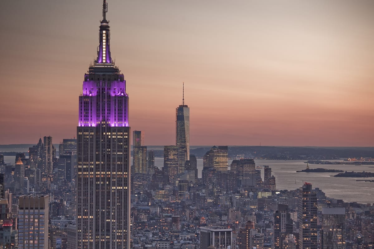 Empire State Building lit up purple with the sunset or sunrise in the background 