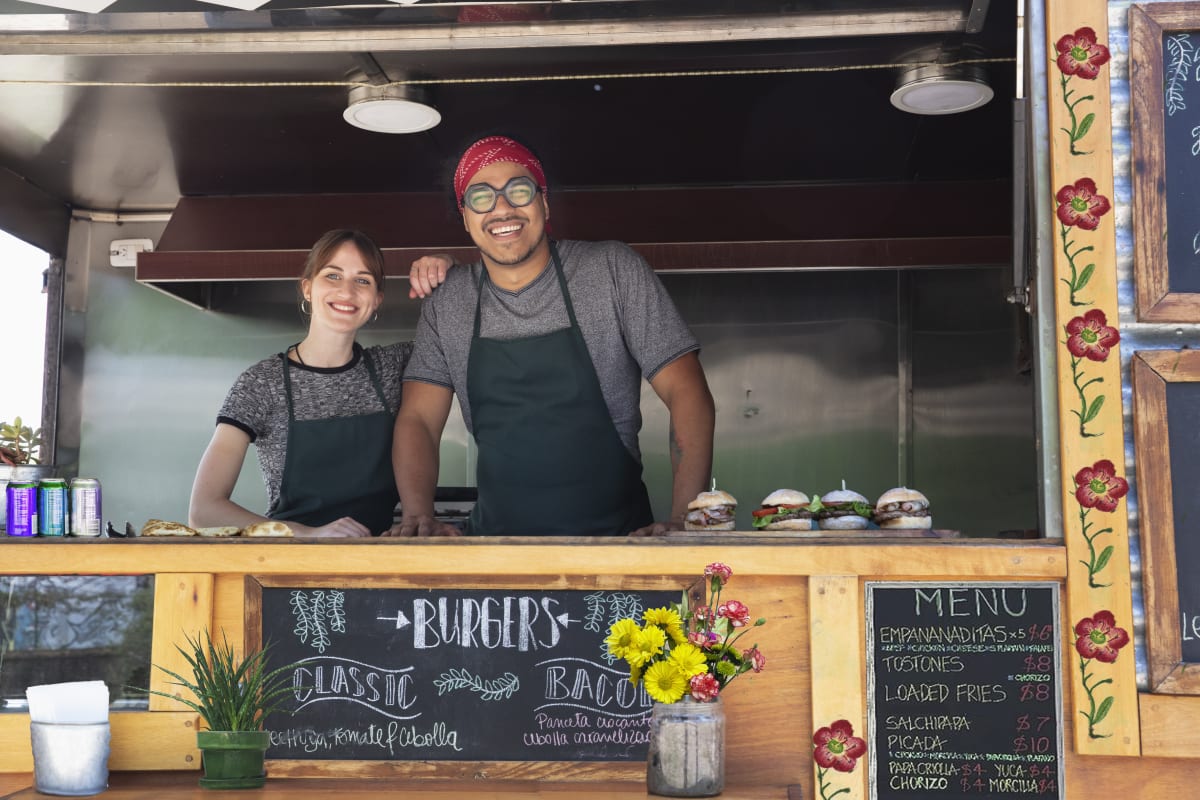 Man and woman smile from inside food truck 