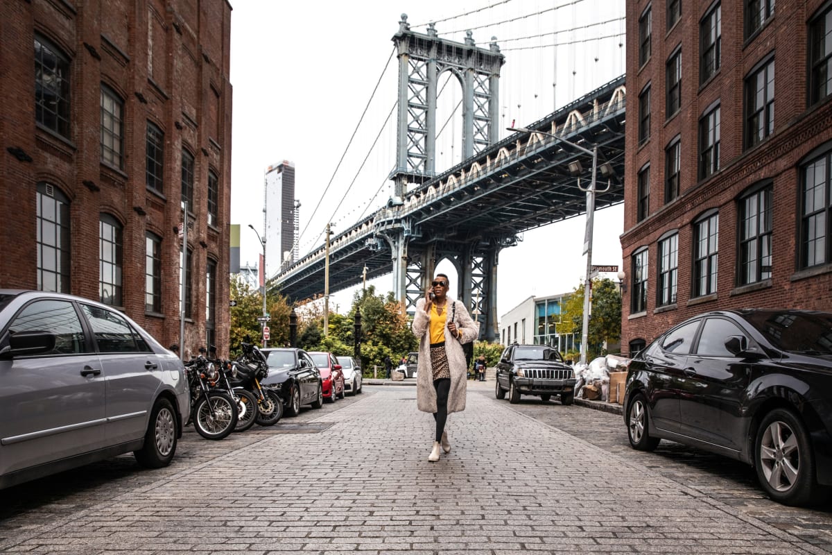 Woman poses in DUMBO district on quiet paved street with Brooklyn Bridge in the background