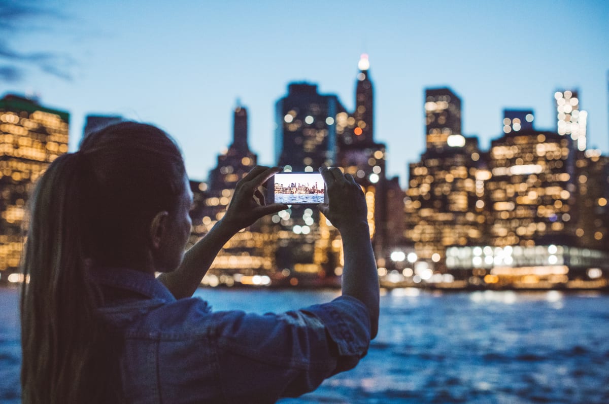 Woman takes photo on her phone of New York city skyline after sunset 