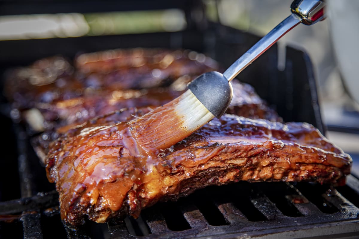 Marinade is applied to ribs on a grill with a brush 