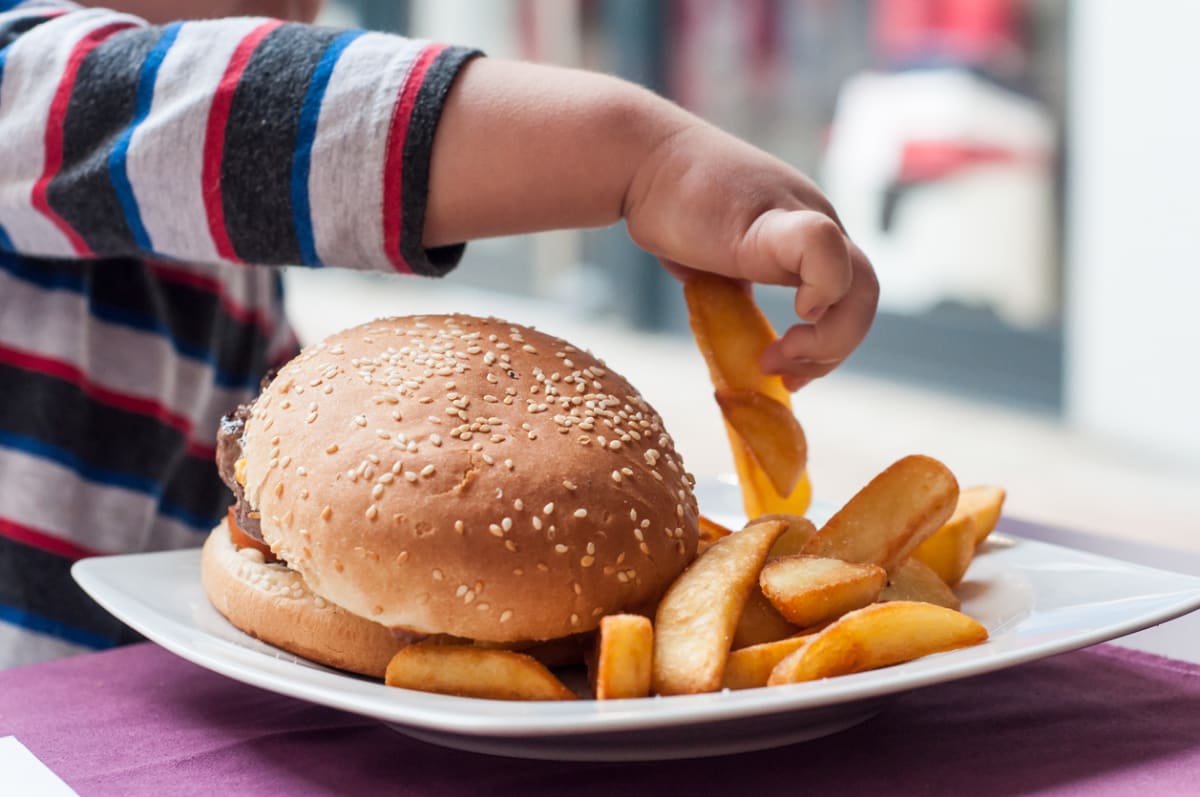 Child picking up a fry from a plate with a burger and fries