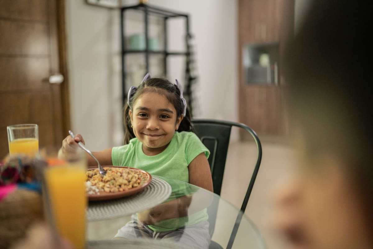 young girl smiles over a plate of food