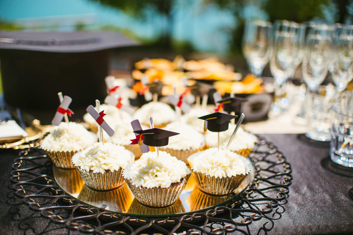 Plate of white iced cupcakes with small graduation hats and scrolls decorations on top  