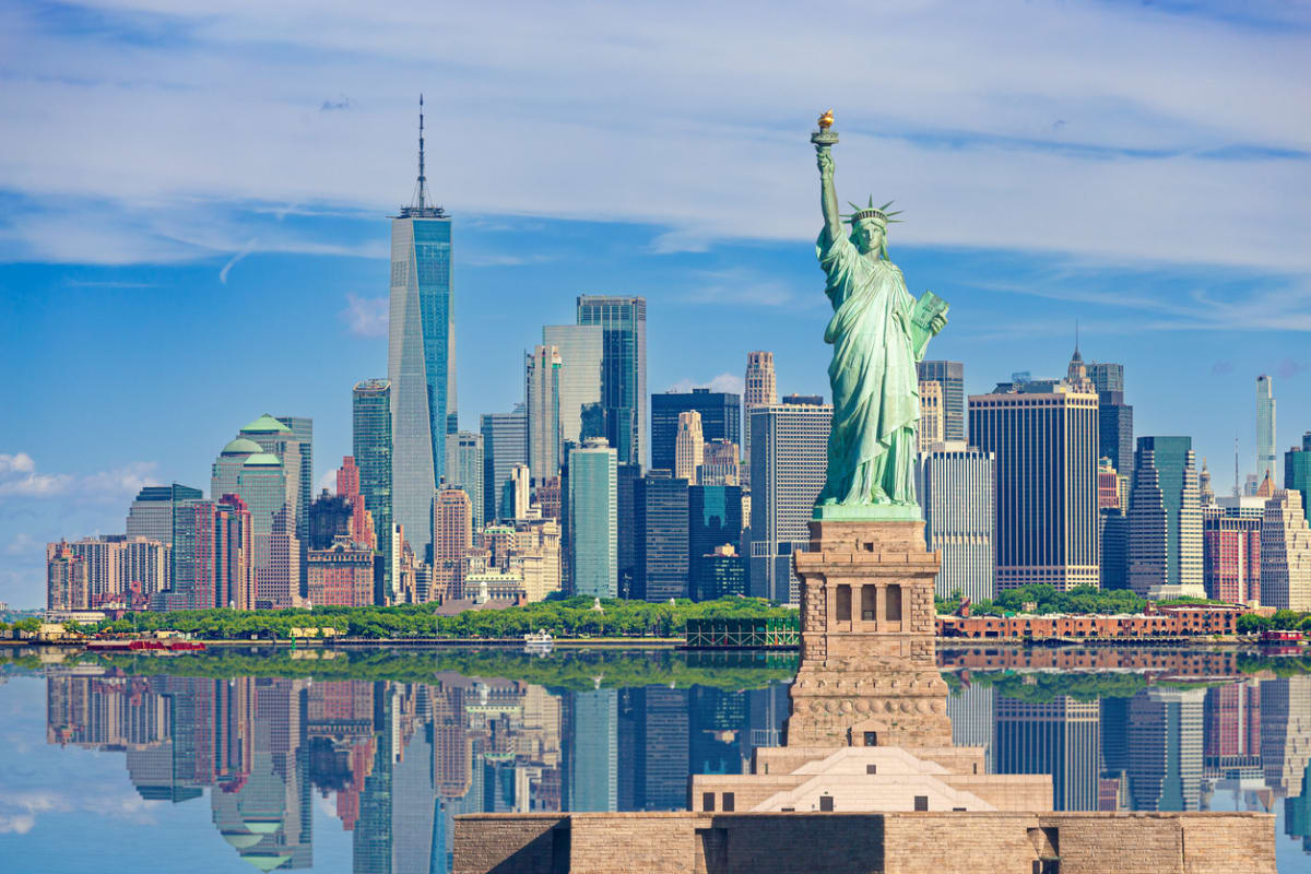 Statue of liberty in front of the new york skyline with blue skies and sunshine