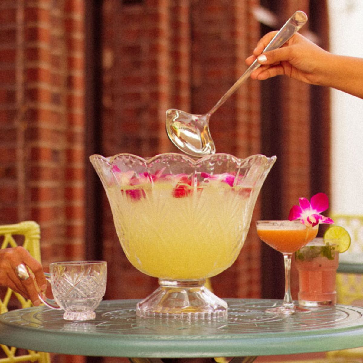 woman-serving-tropical-cocktail-from-large-glass-container-into-small-glass