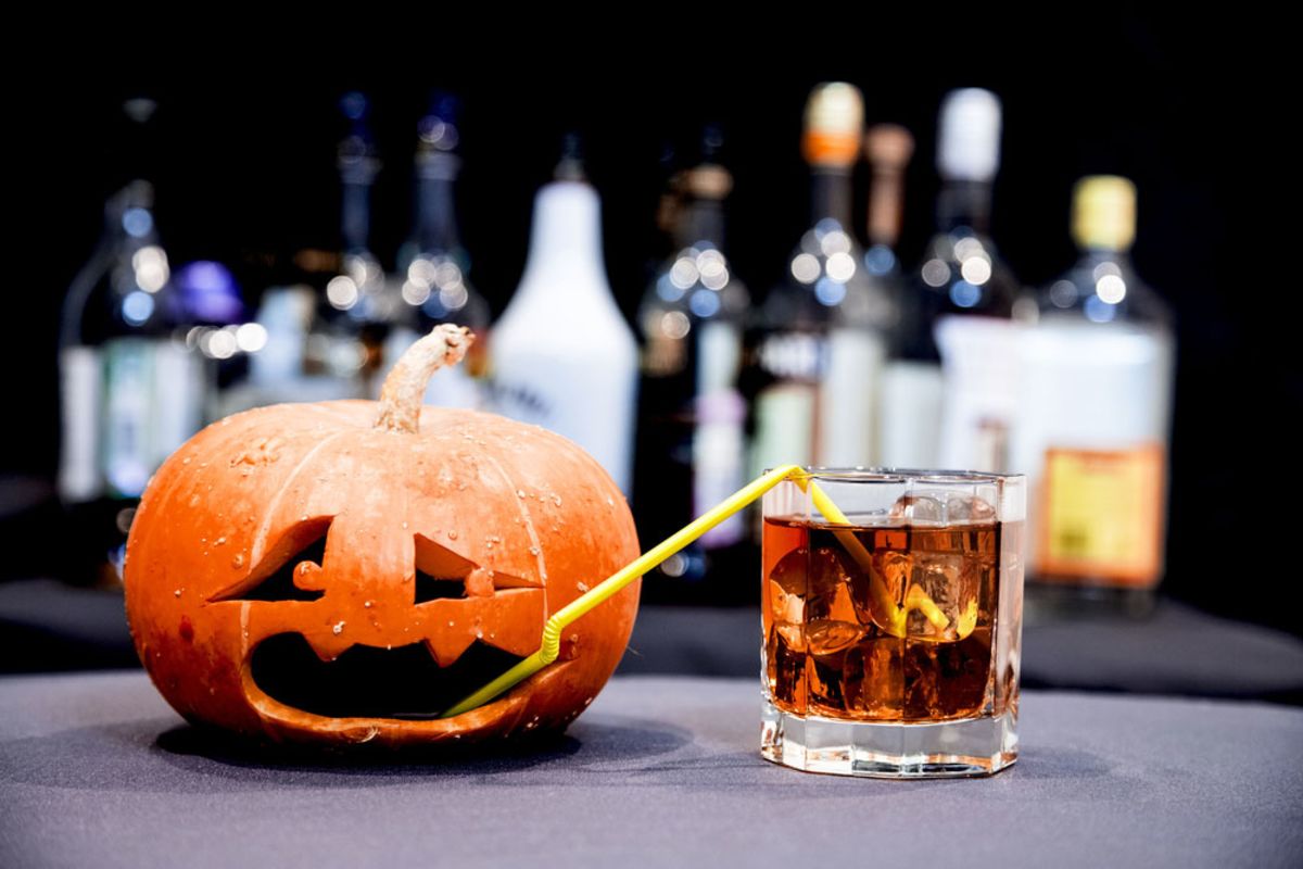 Jack-o-lantern with straw into a glass with spirits. 