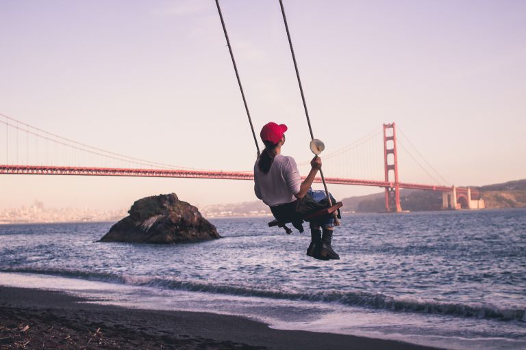 A girl swinging on the beach with bridge in the background