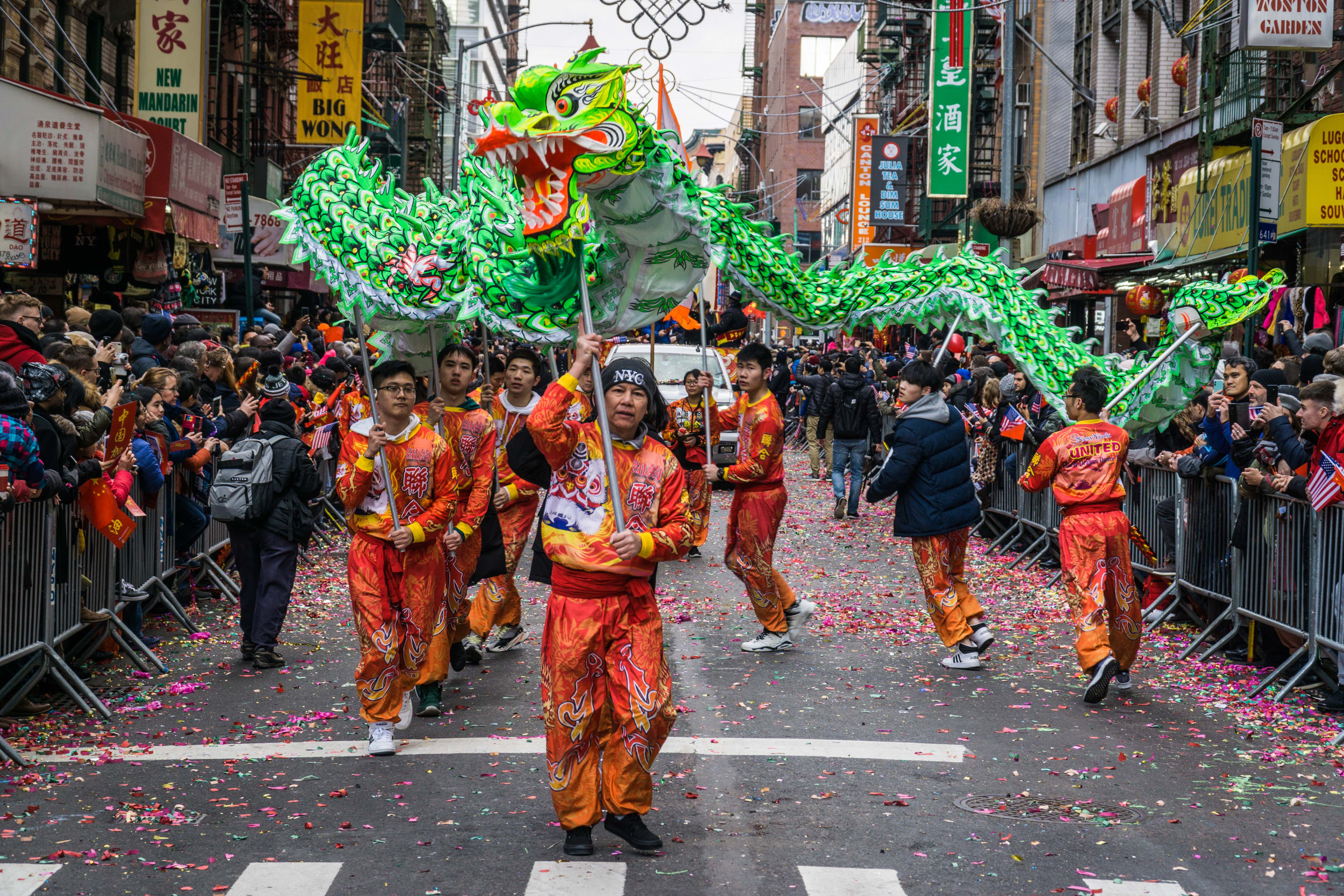 Traditional Chinese dragon dance, with green dragon held above the mens heads, the men are dressed in red clothing and crowds watch from New York China town streets. 