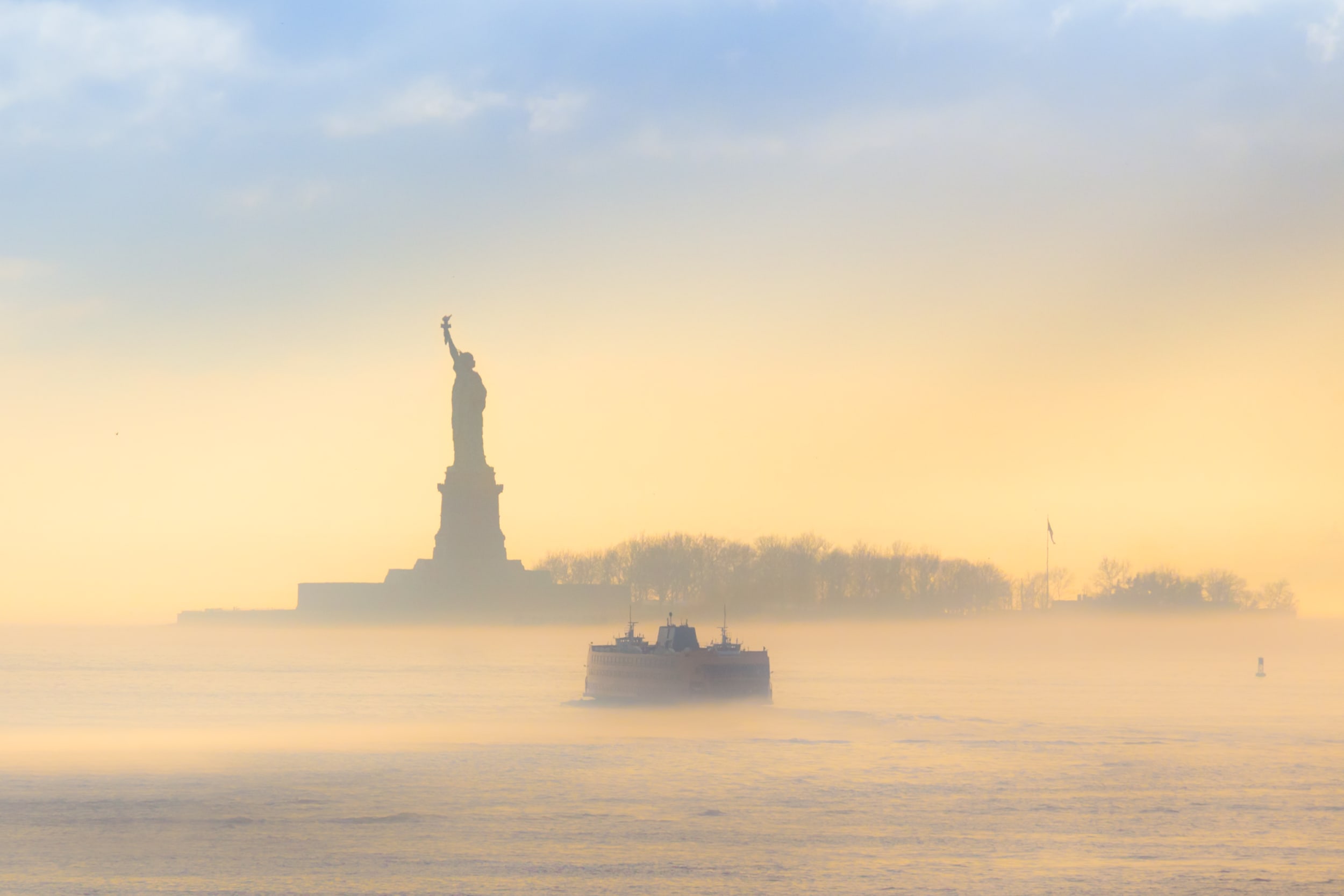 Staten Island Ferry approaches Statue of Liberty, in the fog ay sunrise or sunset 