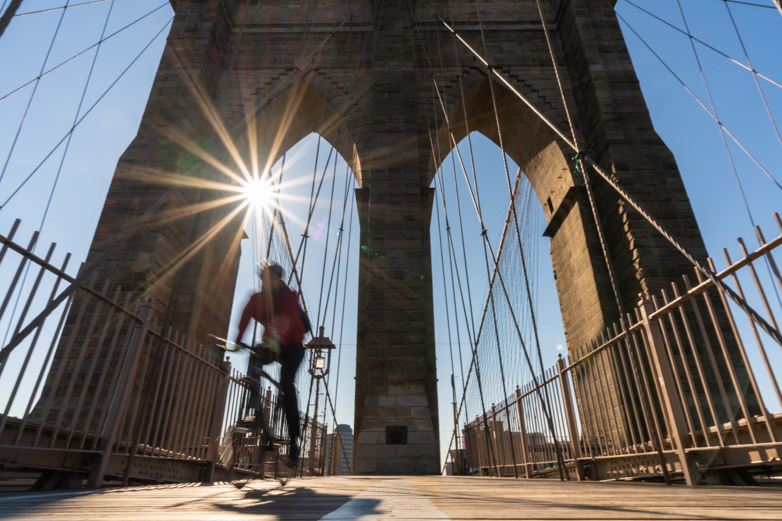 Man rides bike over Manhattan Bridge in the sunlight 