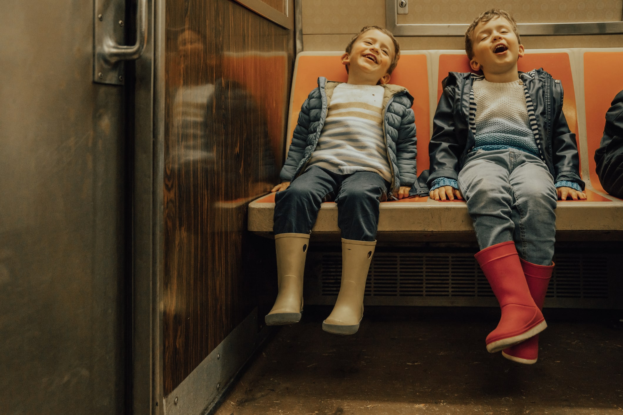 Two young boys in boots and rain coats smile on the subway 