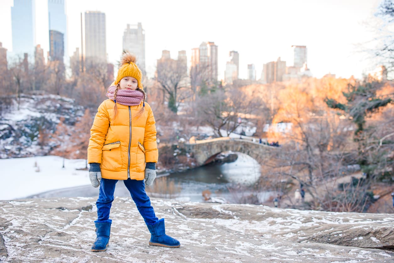 Kid in a yellow jacket and hat in front of Central Park in the snow 