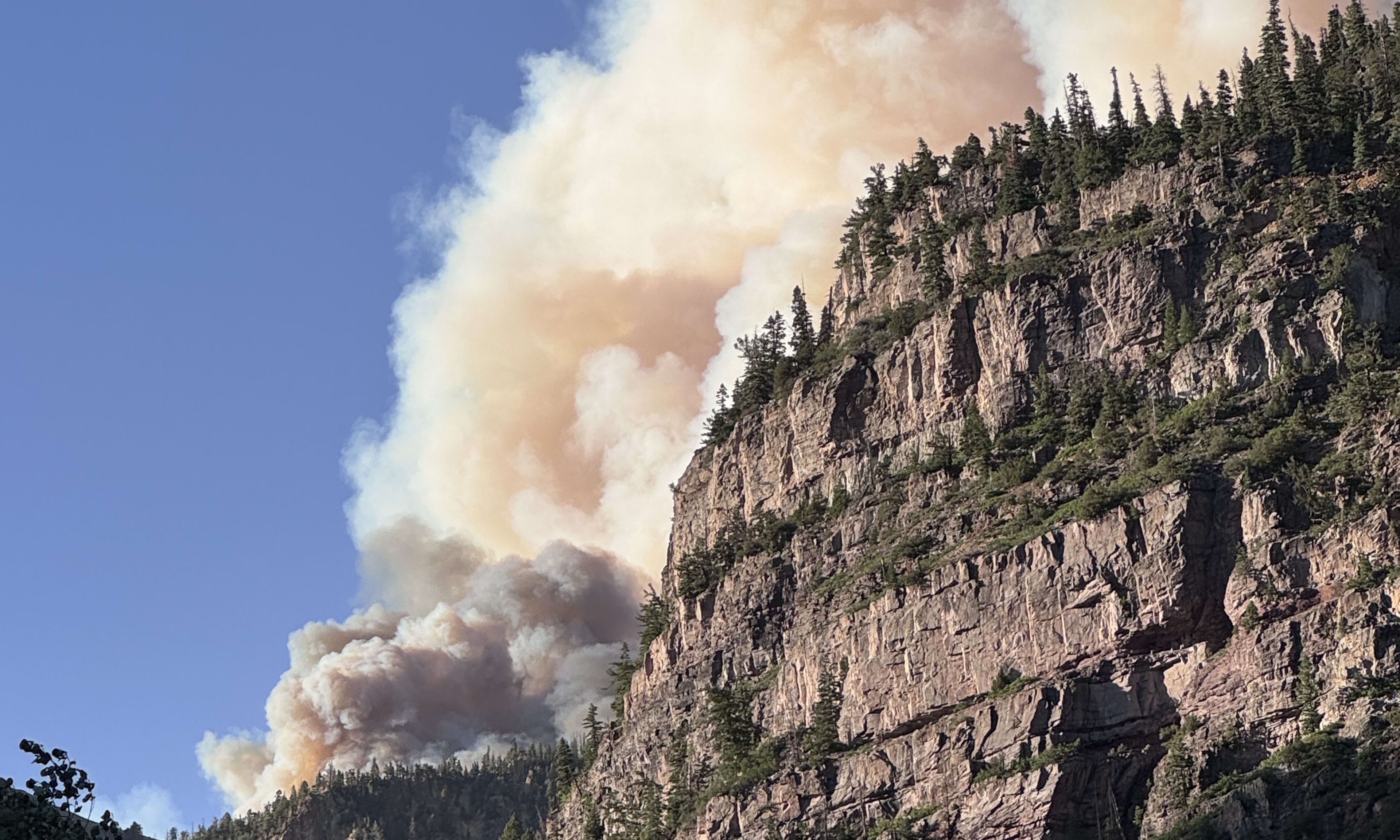 A wildfire smoke plume rising close behind a tall cliff face near Ouray, Colorado