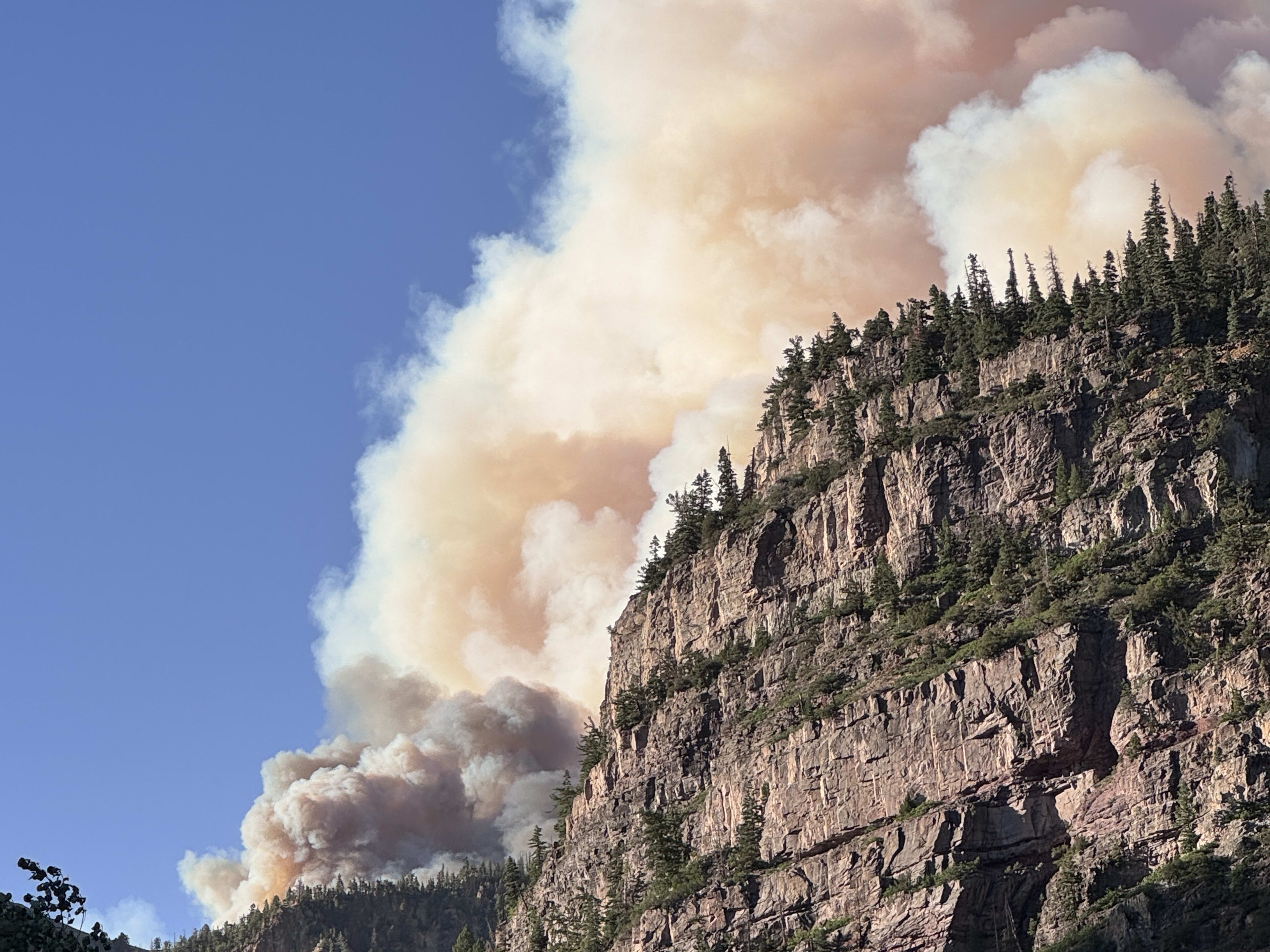 A wildfire smoke plume rising close behind a tall cliff face near Ouray, Colorado