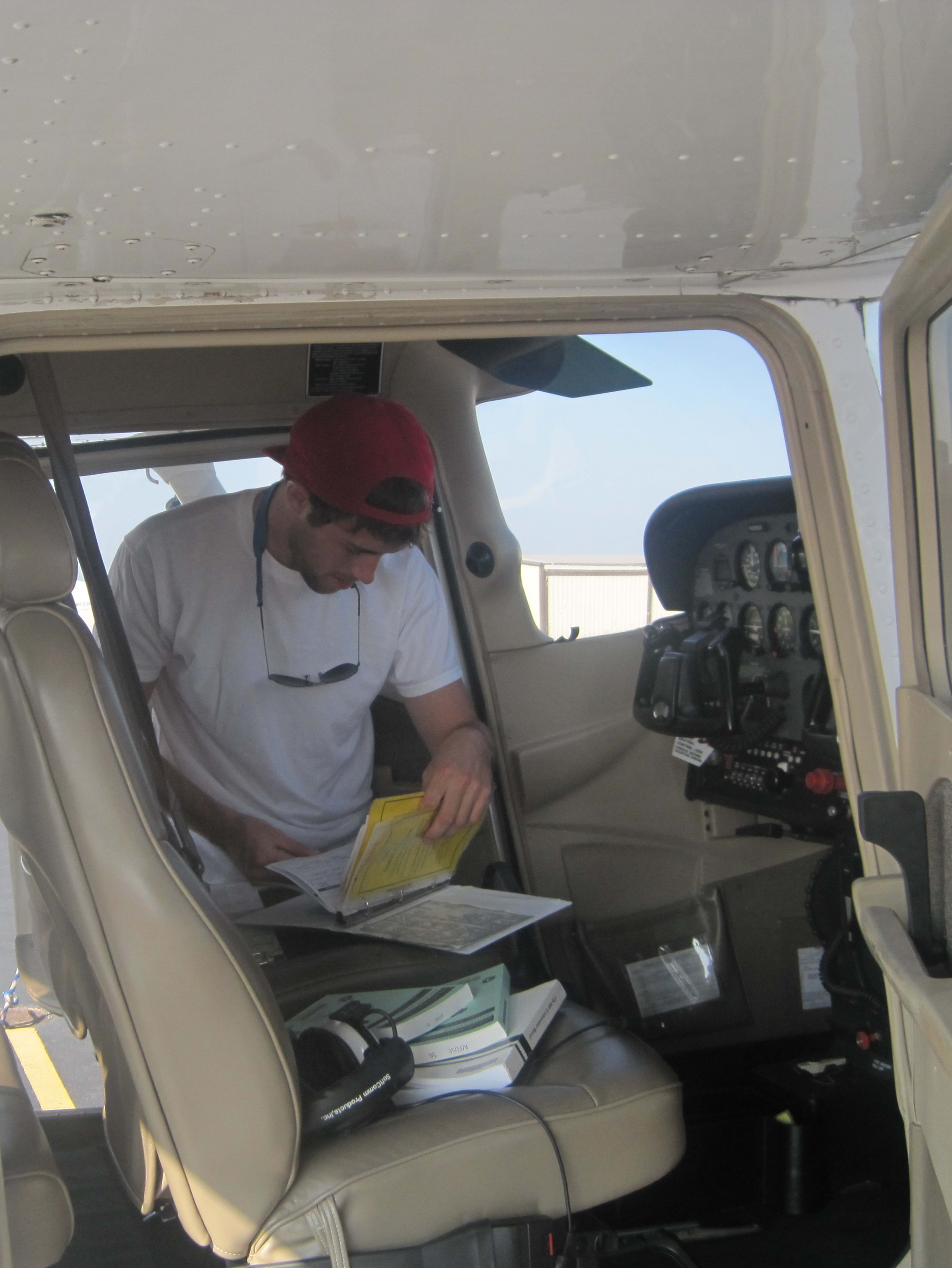 Bret leaning into a Cessna cockpit doing preflight planning with paper charts and books on the seat