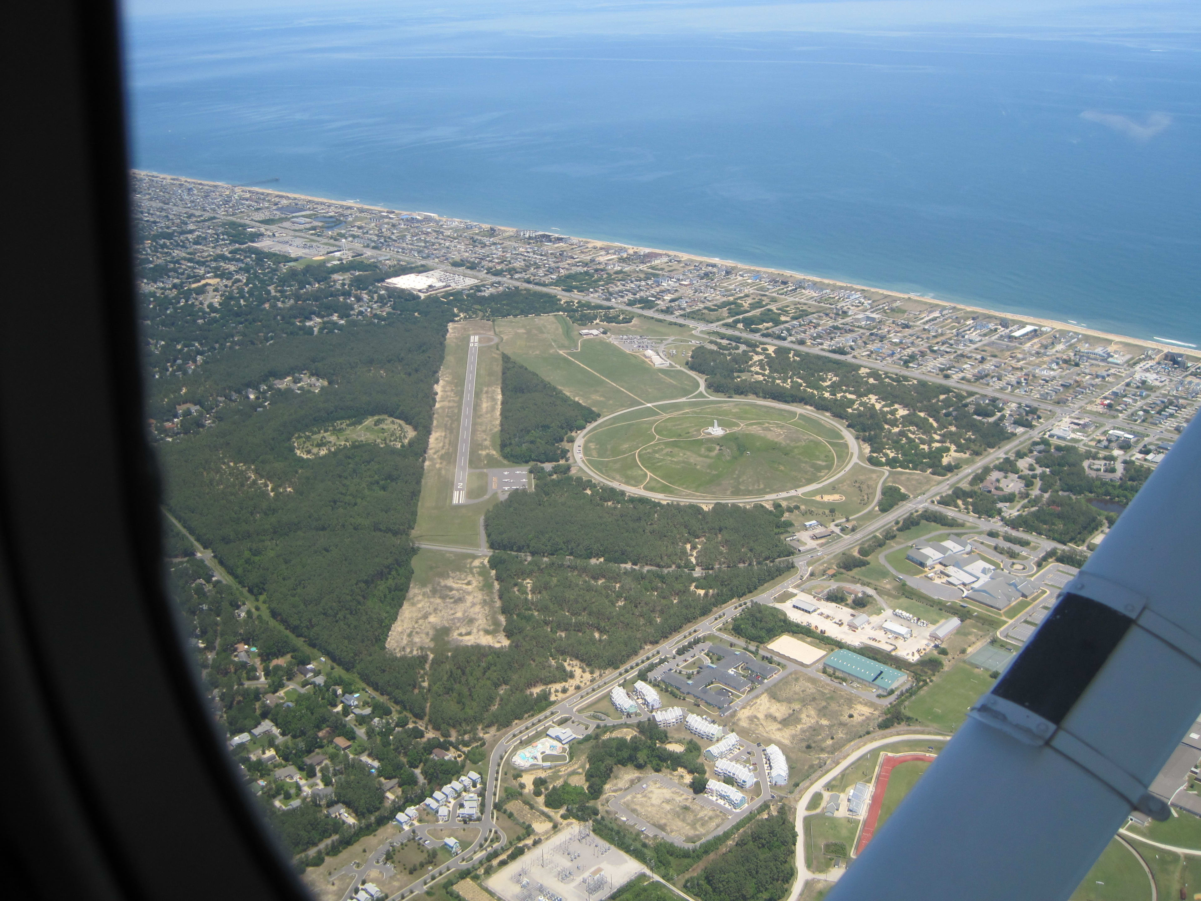 Aerial view through a Cessna window of the Wright Brothers Memorial, runway, and coastline