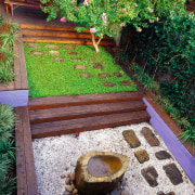 The pond is built into a base of backyard, courtyard, garden, grass, landscape, landscaping, plant, tree, walkway, wood, yard