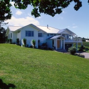 A photograph of a house built on a architecture, backyard, cottage, estate, facade, farmhouse, grass, home, house, land lot, landscape, lawn, neighbourhood, plant, plantation, property, real estate, residential area, rural area, siding, sky, suburb, tree, yard, green