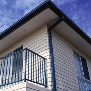 View of the side of this home - architecture, balcony, building, commercial building, daylighting, daytime, facade, home, house, line, real estate, residential area, roof, siding, sky, structure, window, blue, gray