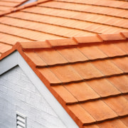 Closeup of terracotta coloured concrete roof tiles on brickwork, daylighting, line, lumber, material, outdoor structure, roof, siding, wood, wood stain, orange