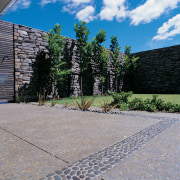 Paved area with exposed aggregate concrete and contrasting architecture, cobblestone, courtyard, driveway, estate, facade, grass, home, house, landscape, landscaping, outdoor structure, plant, real estate, residential area, road surface, sky, stone wall, tree, walkway, wall, gray