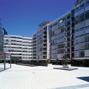 View of paved public plaza bounded by various apartment, architecture, building, city, commercial building, condominium, corporate headquarters, facade, headquarters, metropolis, metropolitan area, mixed use, neighbourhood, property, real estate, residential area, sky, tower block, urban design, blue