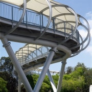 View of curved pedestrian foot bridge showing steel architecture, bridge, building, fixed link, landmark, sky, structure, tree, black