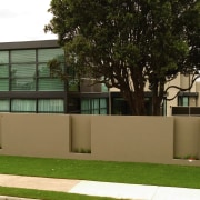 Street frontage of townhouse development with extensive glazing. architecture, building, facade, fence, grass, home, house, neighbourhood, plant, real estate, residential area, tree, brown